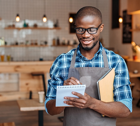 Young handsome Black business owner wearing an apron and checking things off his to-do list.