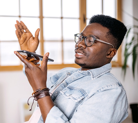 Young Black business owner in a denim shirt and glasses talking on his phone while sitting at his desk.